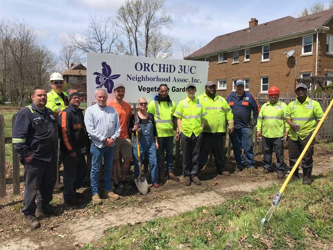 People smiling for a picture, wearing construction vents and woman in center holding a shovel